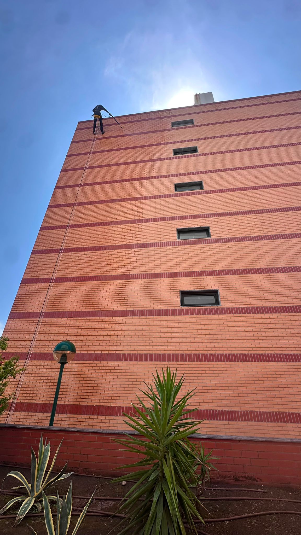 Profissional a realizar limpeza de telhado em rappel através de técnicas de acesso por cordas